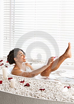 Pretty black young woman shaving legs while taking bath