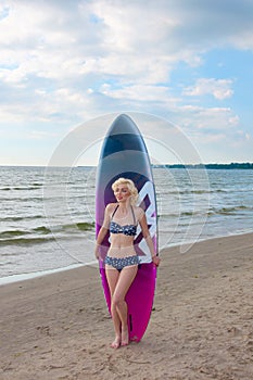 Pretty blond girl model like Marilyn Monroe with surfing board on a beach