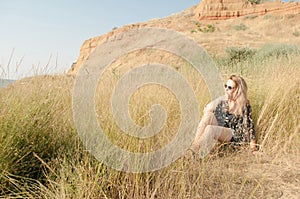 Pretty blond girl sitting on field with dry grass.