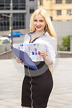Pretty blond secretary writes somthing on documents outdoors.