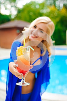 Pretty blond woman enjoying cocktail near a swimming pool