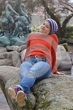 Pretty blond woman with knit cap sitting in a park on a rock