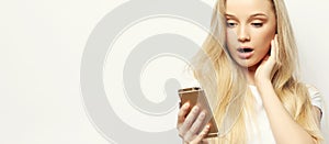 Pretty blond woman with long hair holds modern smart phone, recieves unexpcted message from friend, reads reminder photo