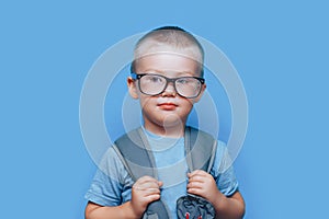 Pretty blonde boy on blue background with backpack unhappy, sad, child don`t want go to school. back to school