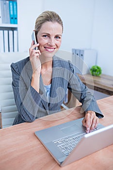 Pretty blonde businesswoman phoning and using her laptop