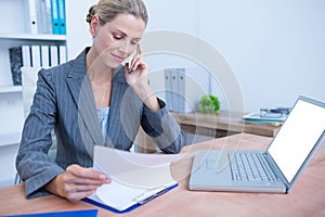 Pretty blonde businesswoman phoning and using her laptop