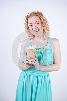 Pretty blonde caucasian woman wearing long blue summer dress holding paper cup of coffee and enjoys life on white studio backgroun