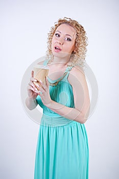 Pretty blonde caucasian woman wearing long blue summer dress holding paper cup of coffee and enjoys life on white studio backgroun