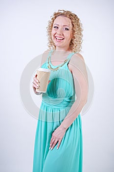 Pretty blonde caucasian woman wearing long blue summer dress holding paper cup of coffee and enjoys life on white studio backgroun