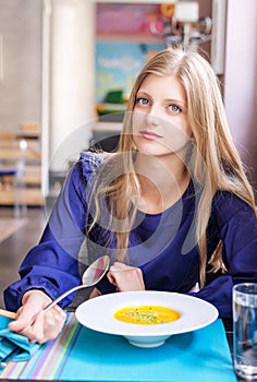 Pretty blonde girl eating pumpkin soup in restaurant