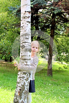 Pretty blonde girl with flowers hugging the birch tree