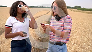 Pretty blonde girl and mixed race teenager young women wearing sunglasses drinking coffee and taking selfies on their smart phones