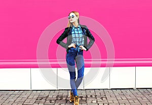 Pretty blonde girl model in full-length posing wearing rock black style jacket, hat on city street over colorful pink wall