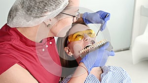 Pretty blonde girl in protective yellow glasses on the stamotologist examined her open mouth. Female dentist examines