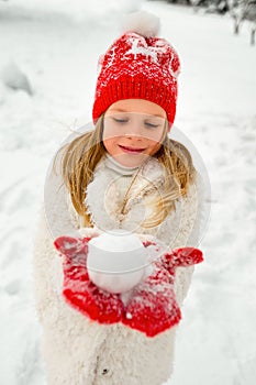 Pretty blonde girl in a red hat and knitted mittens plays with snow. winter portrait