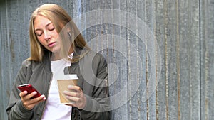 Pretty blonde girl teenager young woman using her smartphone or cell phone for social media and drinking takeout coffee