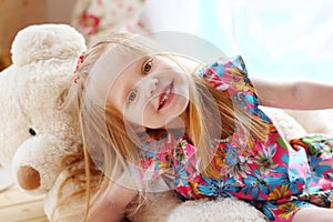 Pretty blonde little girl lies on big soft toy bear