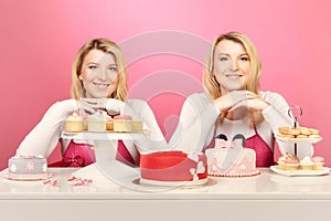 Pretty blonde twins with desserts and cakes on pink