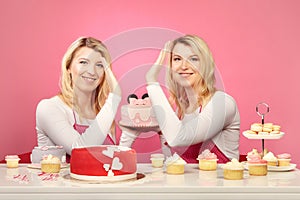 Pretty blonde twins with desserts and cakes on pink