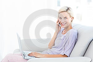 Pretty blonde woman calling on the phone and using her laptop