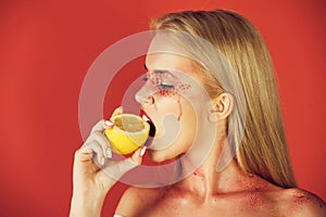Pretty blonde woman with creative fashionable makeup bite lemon, vitamin