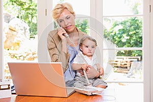 Pretty blonde woman with his son phoning and using laptop