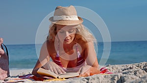 Pretty blonde woman lying on towel and reading book