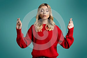 Pretty blonde woman posing isolated on blue background. Waiting for special moment, keeping fingers crossed, making wish