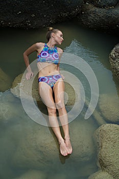 Pretty blonde woman between rocks near the sea during beautiful summer day