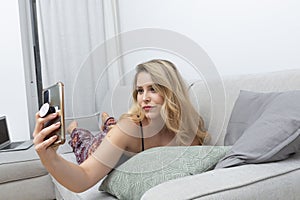 pretty blonde woman taking photos with her smart-phone on the sofa in her living room