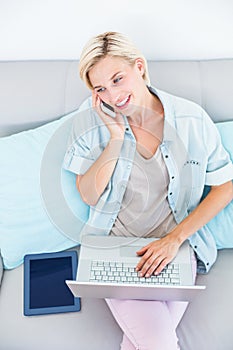 Pretty blonde woman using her laptop while calling on the phone