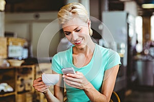 Pretty blonde woman using her smartphone with a cup of coffee