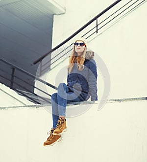 Pretty blonde woman wearing a jacket, hat and sunglasses sitting