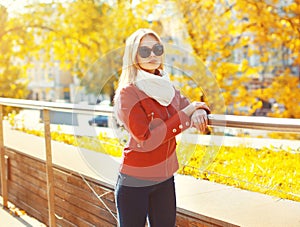 Pretty blonde woman wearing sunglasses and red jacket with scarf in sunny autumn