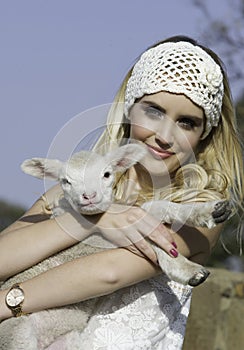 Pretty blonde woman with white crochet headband holding little lamb