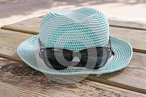 A pretty blue hat and sunglasses lie on the wooden surface.