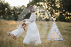 Pretty boho mom whirls her cute daughter. Teepee tent on the background