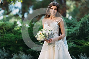 Pretty bride with beautiful bouquet of flowers in hands. Attractive young woman in white dress with wedding make-up on