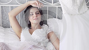 Pretty bride lies on bed and looks at wedding dress