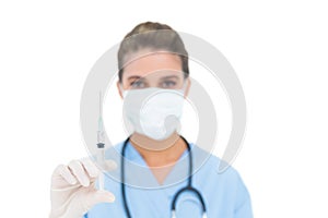 Pretty brown haired nurse in blue scrubs wearing a protection mask and holding a syringe