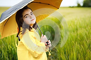 Pretty brunette girl standing in a field with an umbrella in her hands