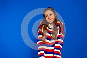 Pretty brunette Hispanic girl about 12 years old shyly posing on blue studio background, she is shrugging her shoulders