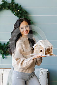 A pretty brunette holds in her hands a gingerbread house prepared with her own hands for Christmas