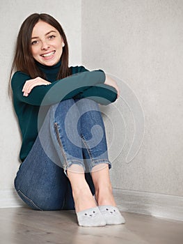 Pretty brunette woman with magnificent eyes and adorable smile in green sweater and blue jeans relaxing sitting on floor hugging
