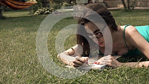 Pretty brunette laying on the lawn and drawing. 4K steadicam wide shot, bleached colors