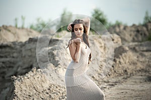 Pretty brunette in light dress stands barefoot on the beach