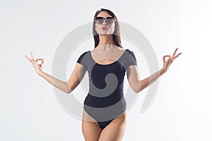 Pretty brunette with long hair, wearing black one piece swimwear, holding hands aside, imitating meditation, making duck