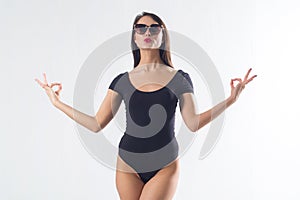 Pretty brunette with long hair, wearing black one piece swimwear, holding hands aside, imitating meditation, making duck photo