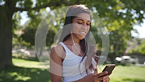 Pretty brunette mixed race young woman listening to music on earphones texting chatting with her friends on mobile phone