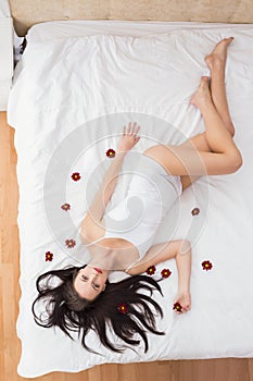 Pretty brunette posing in bed with flowers